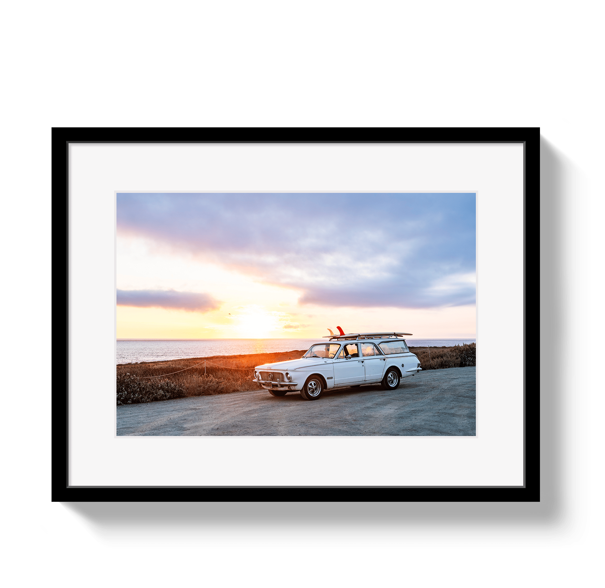 Framed photograph of a vintage car with a surfboard on a beach at sunset.