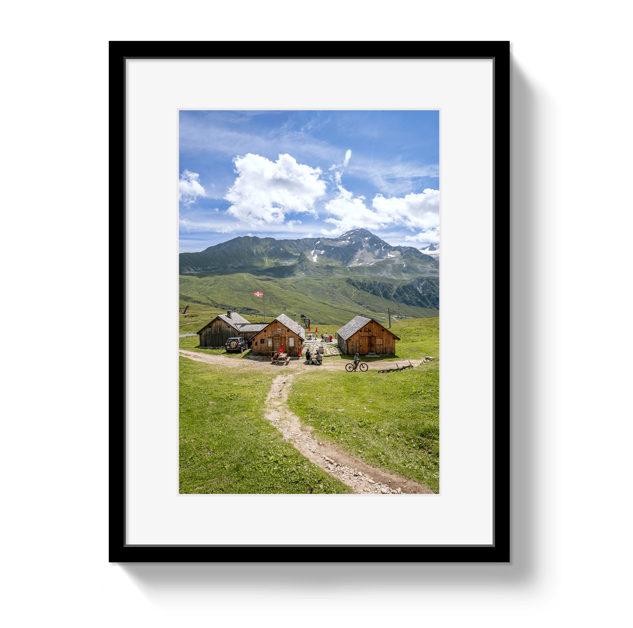 Framed picture of a mountain landscape with wooden cabins and a dirt path.