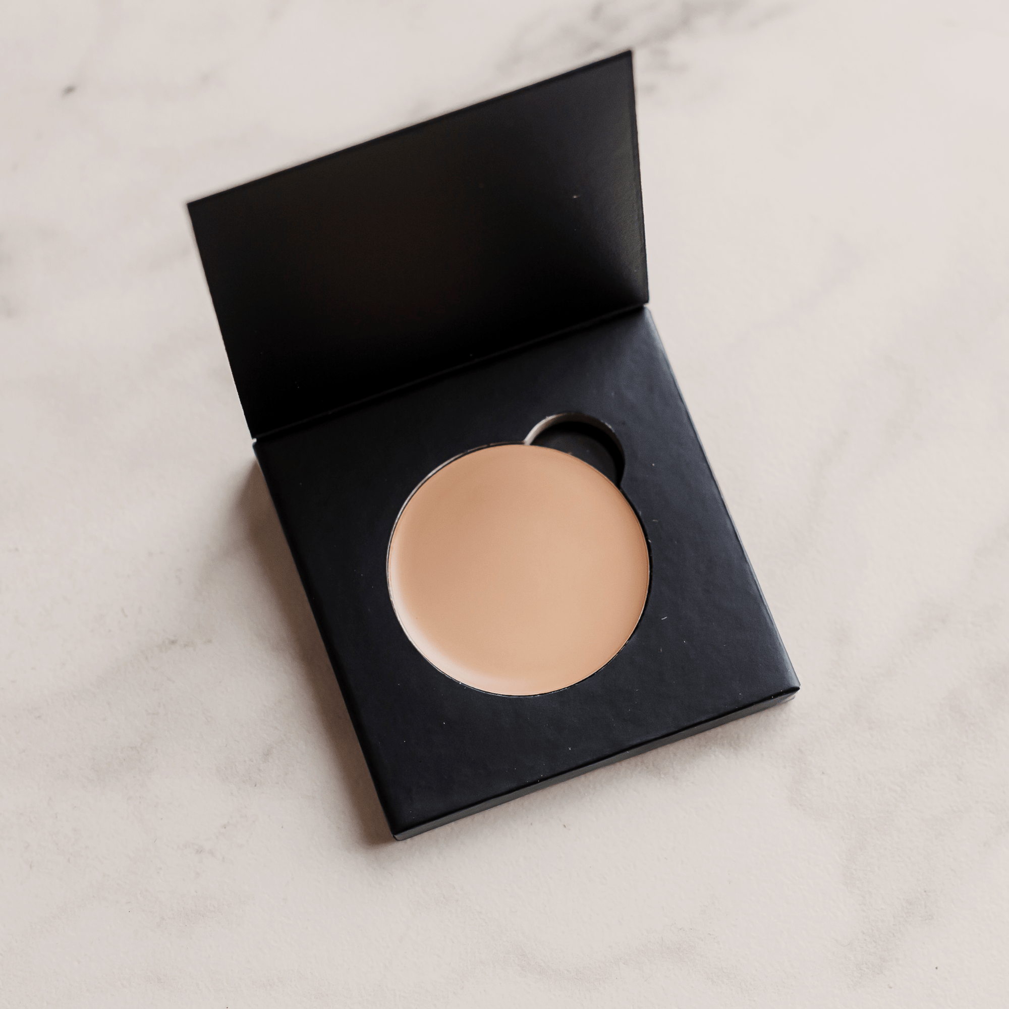 Compact powder in a black case on a light marble background