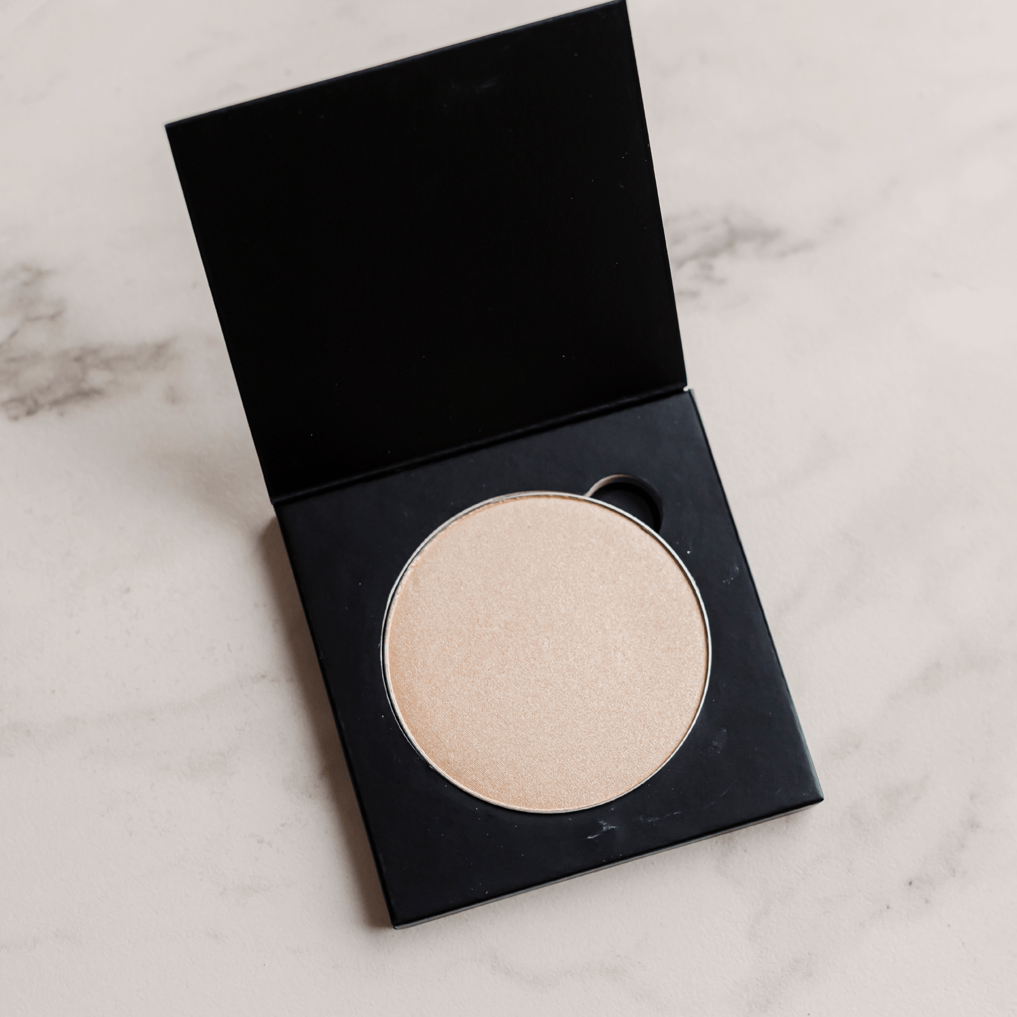 Compact powder in a black case on a marble surface