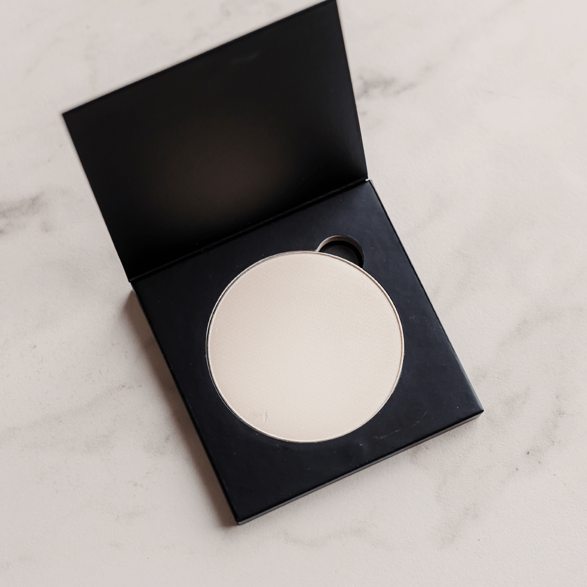 Round compact mirror in a black case on a light marble surface