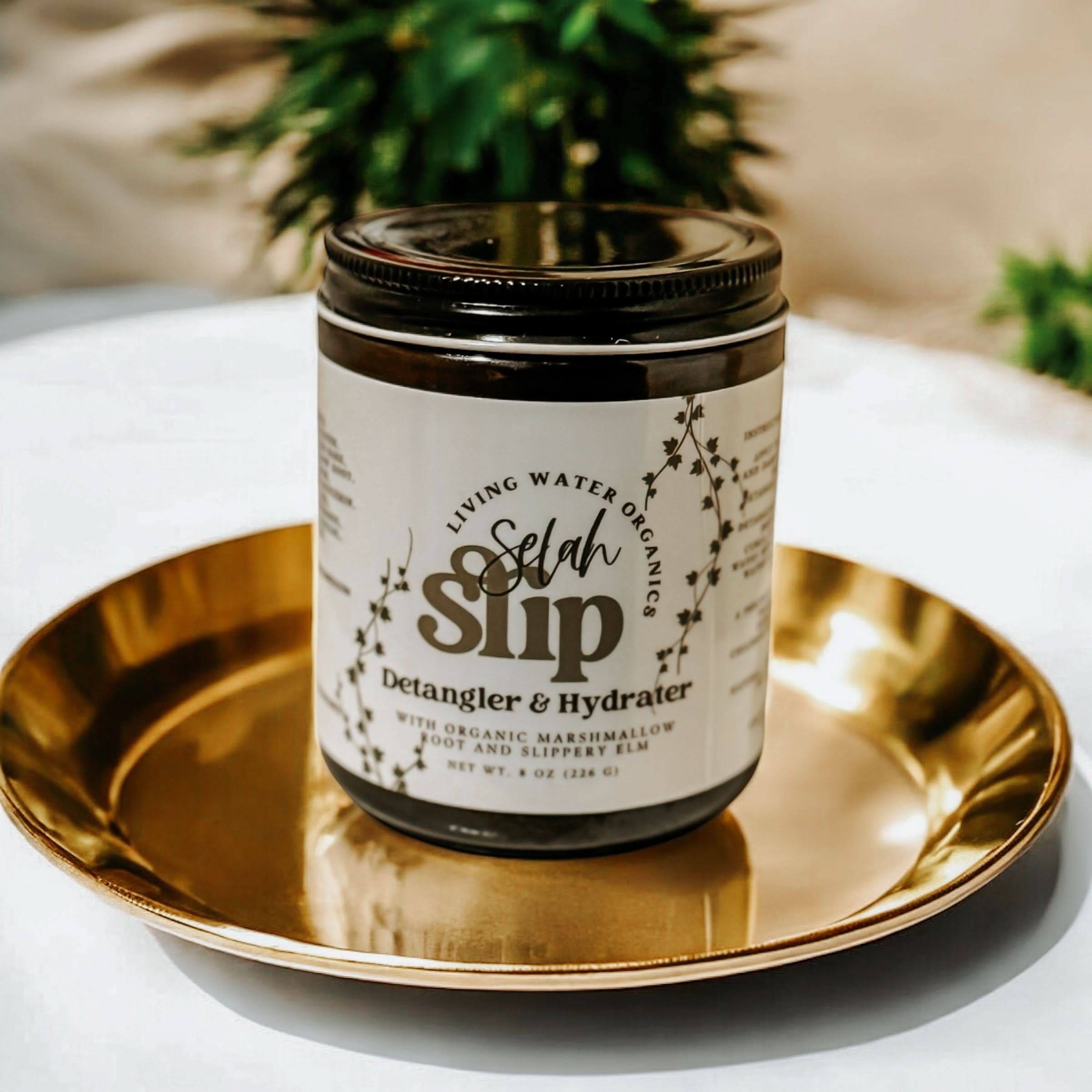Jar of Selah Slip Detangler & Hydrater on a gold plate with a blurred plant in the background