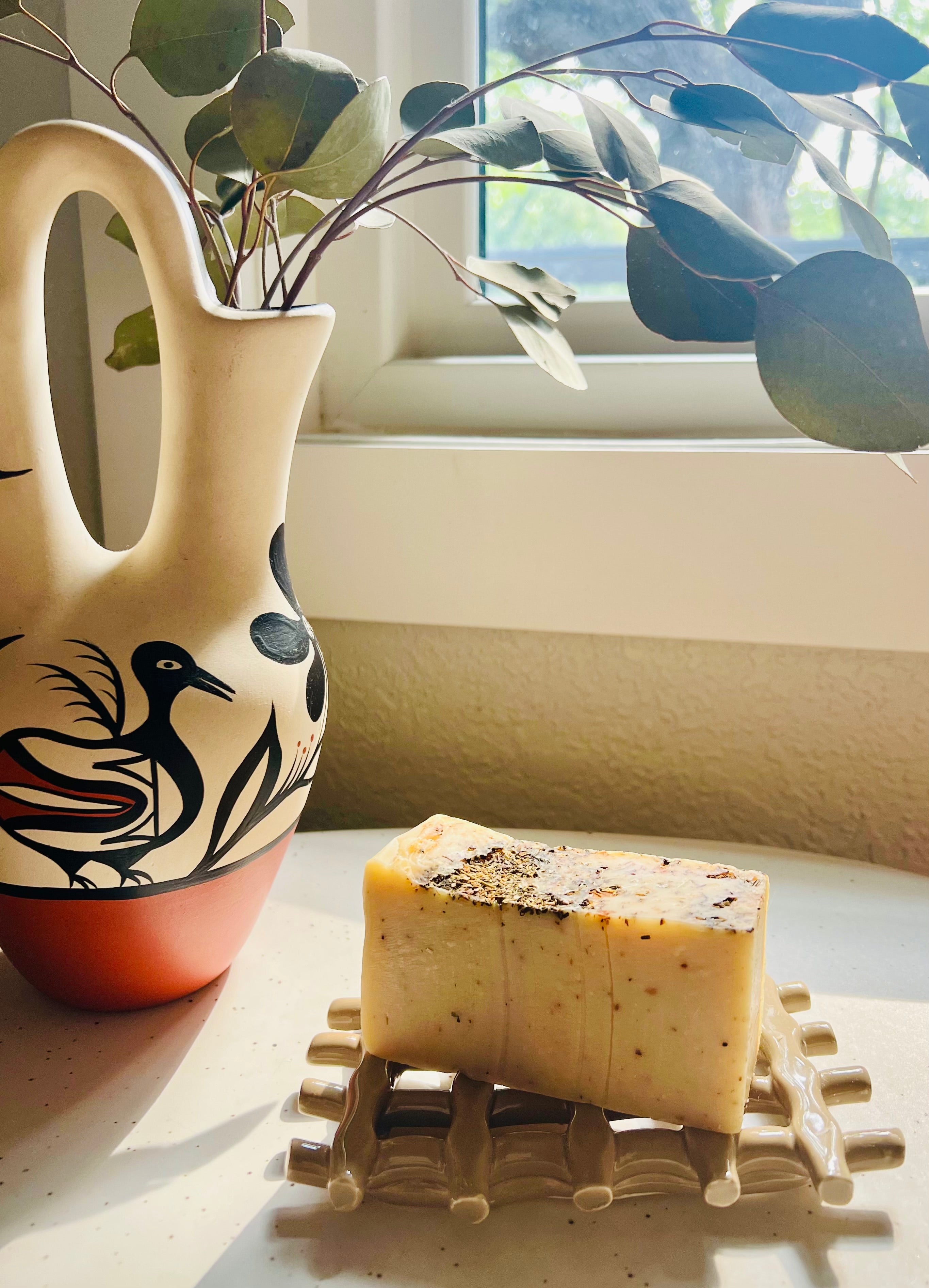 Bar of soap on a decorative stand with a ceramic vase and plant in the background