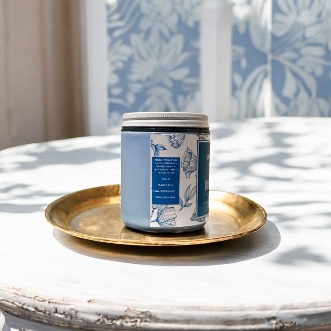 Candle jar with blue label on a gold tray in front of a window with leaf patterned curtains
