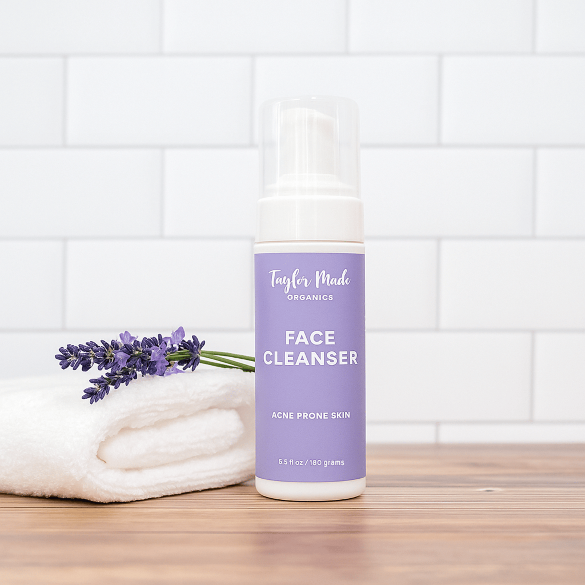 Face cleanser bottle with lavender flowers on a wooden surface and tiled wall background