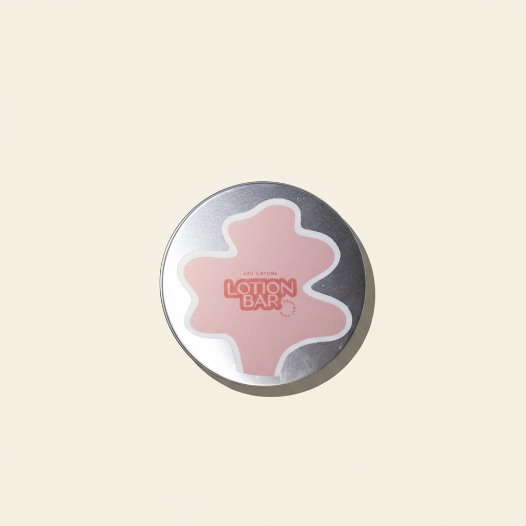 Round lotion bar with pink center and silver casing on a white background