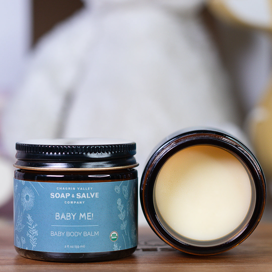 Baby body balm jar with open lid on a wooden surface, featuring the &