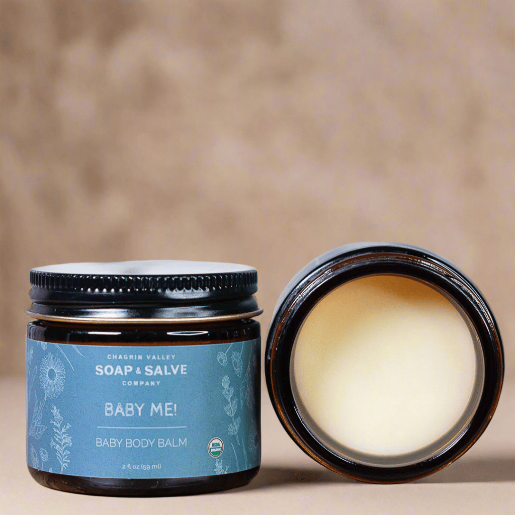 Baby body balm jar with open lid showing cream inside, on a beige background