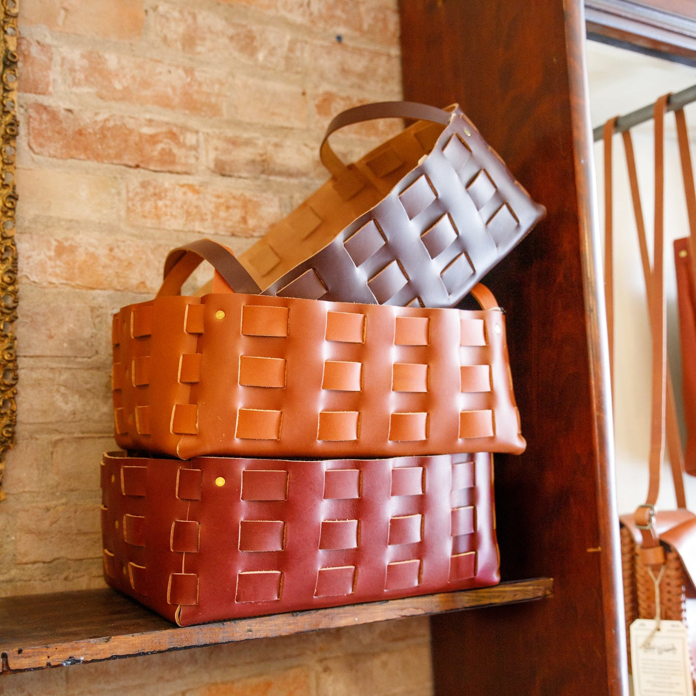 Three woven leather baskets of different sizes on a wooden shelf.