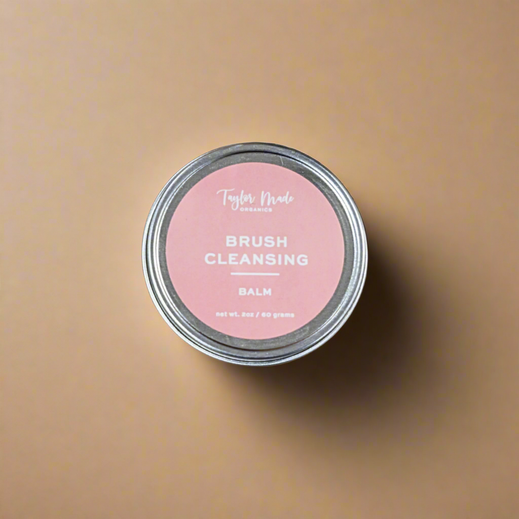 Tin of brush cleansing balm with pink label on a beige background