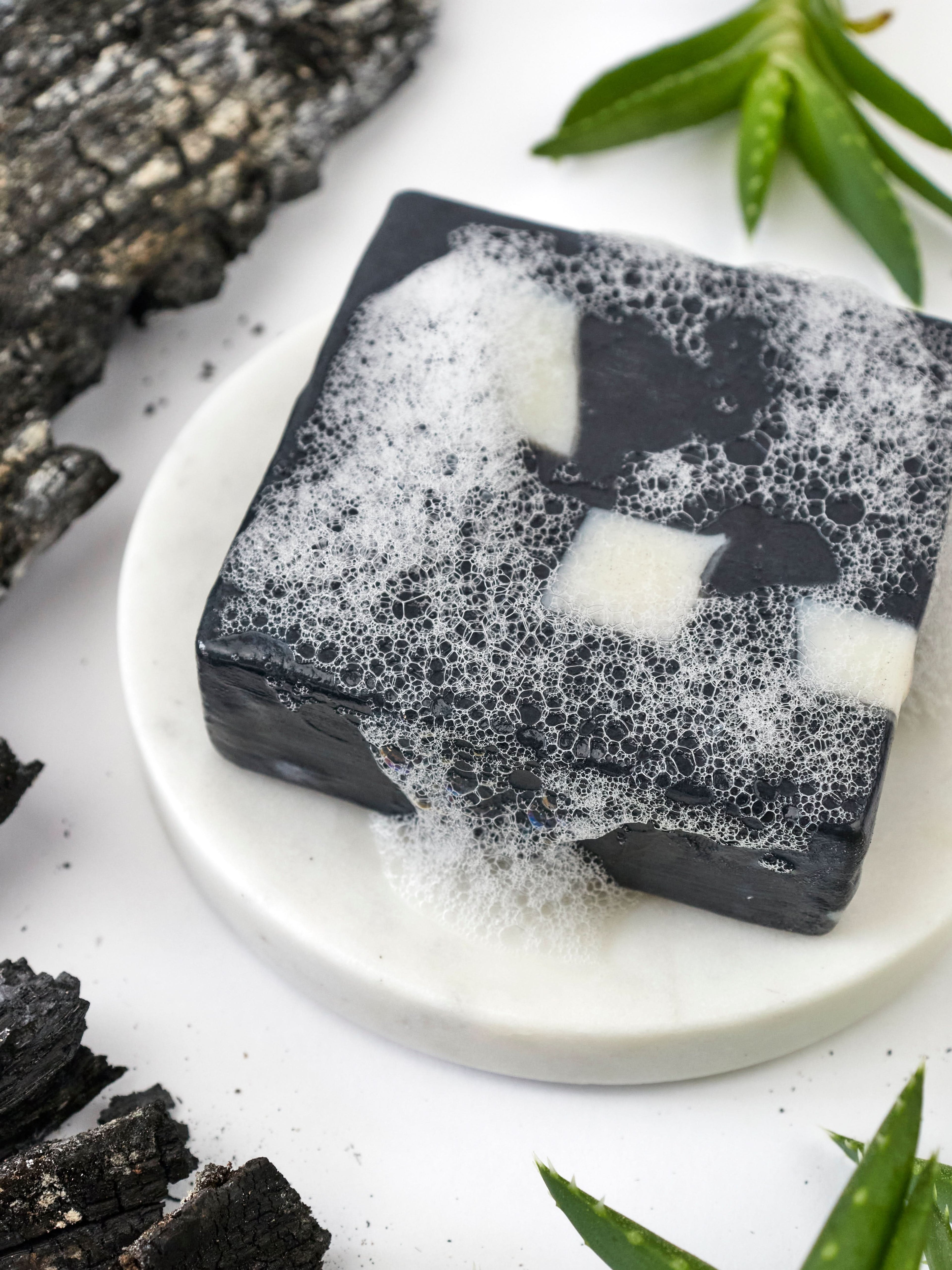 Black and white soap bars on a white plate with green leaves in the background