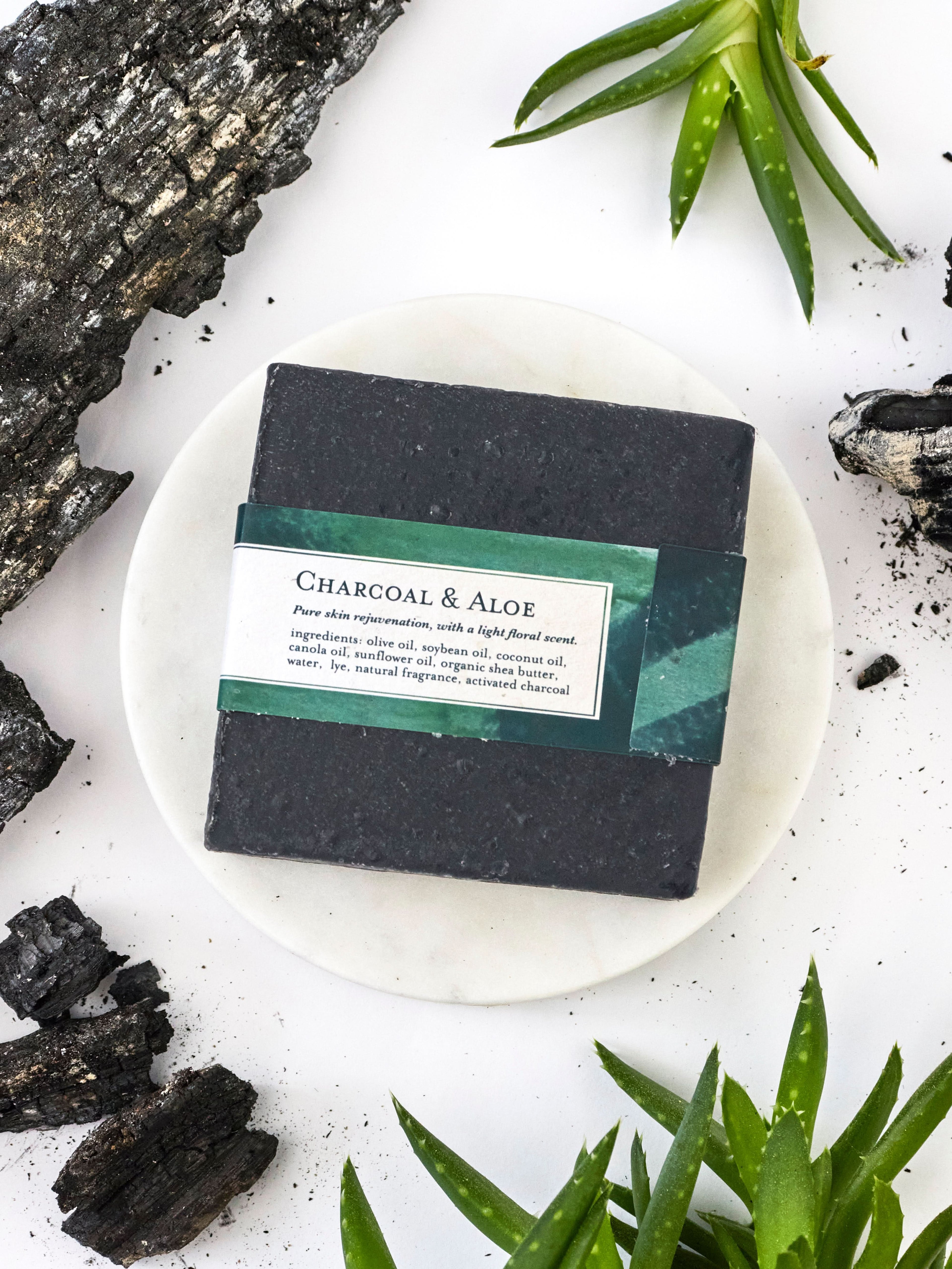 Bar of charcoal and aloe soap on a white plate with natural elements around