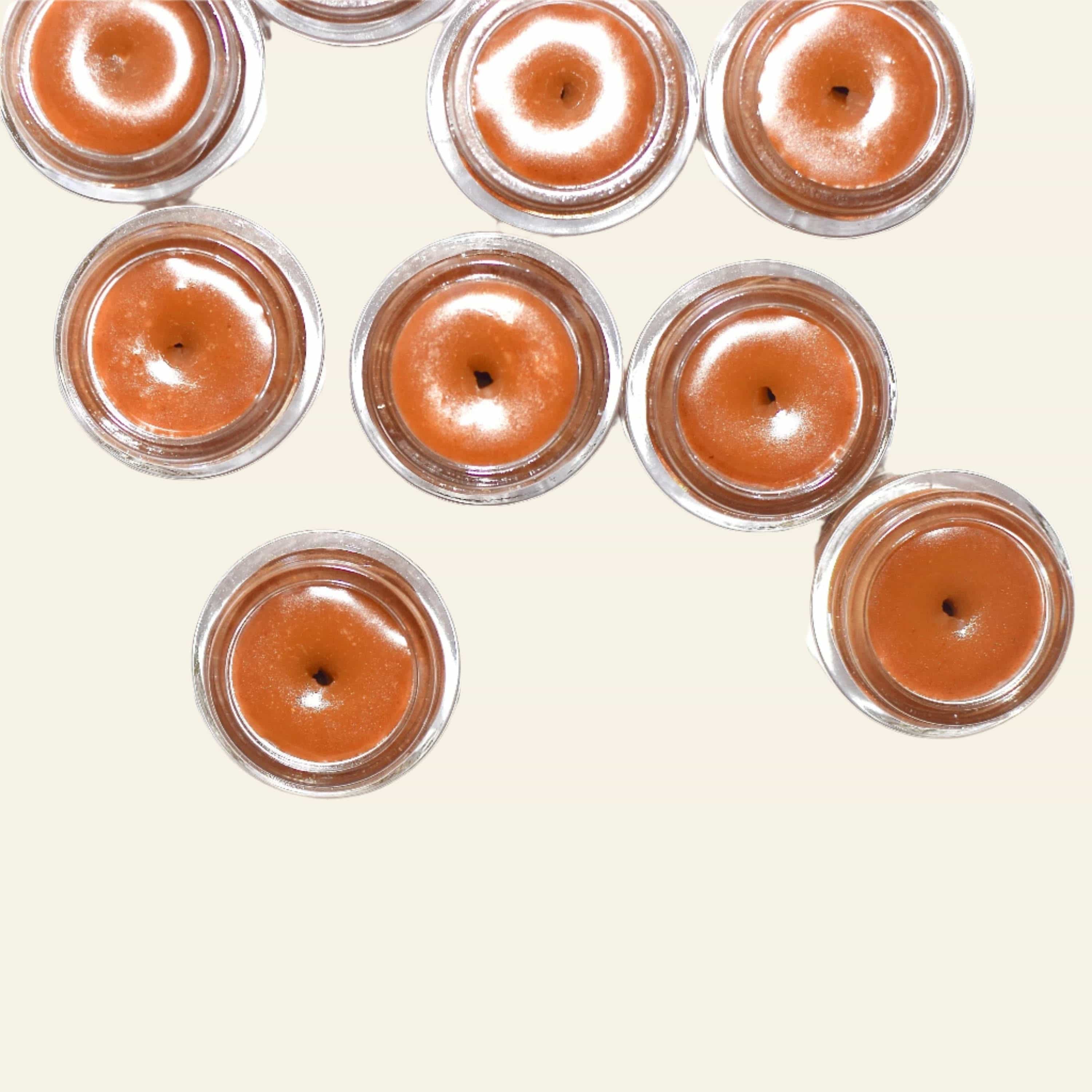 Multiple small jars of a brown cosmetic product on a white background