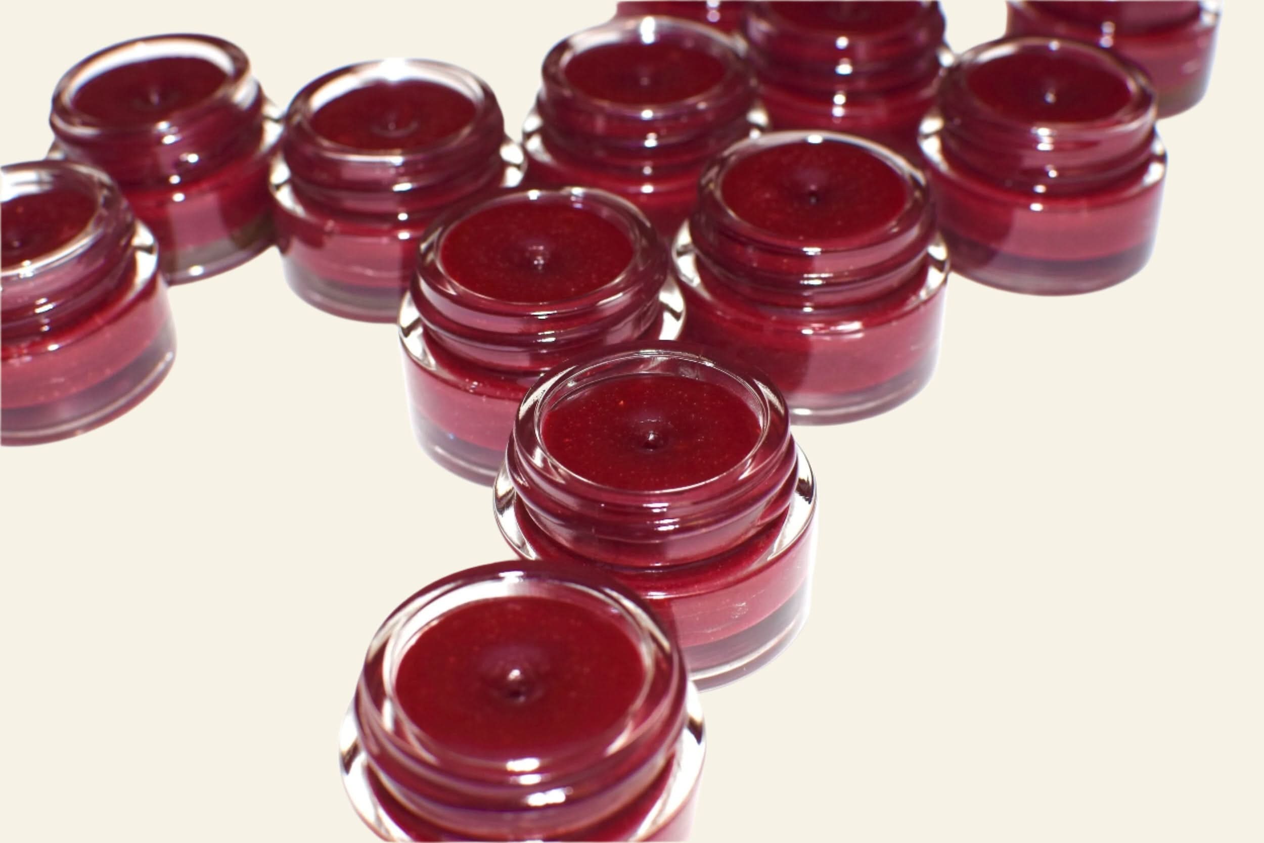 Multiple small jars of red cream or gel arranged on a white background