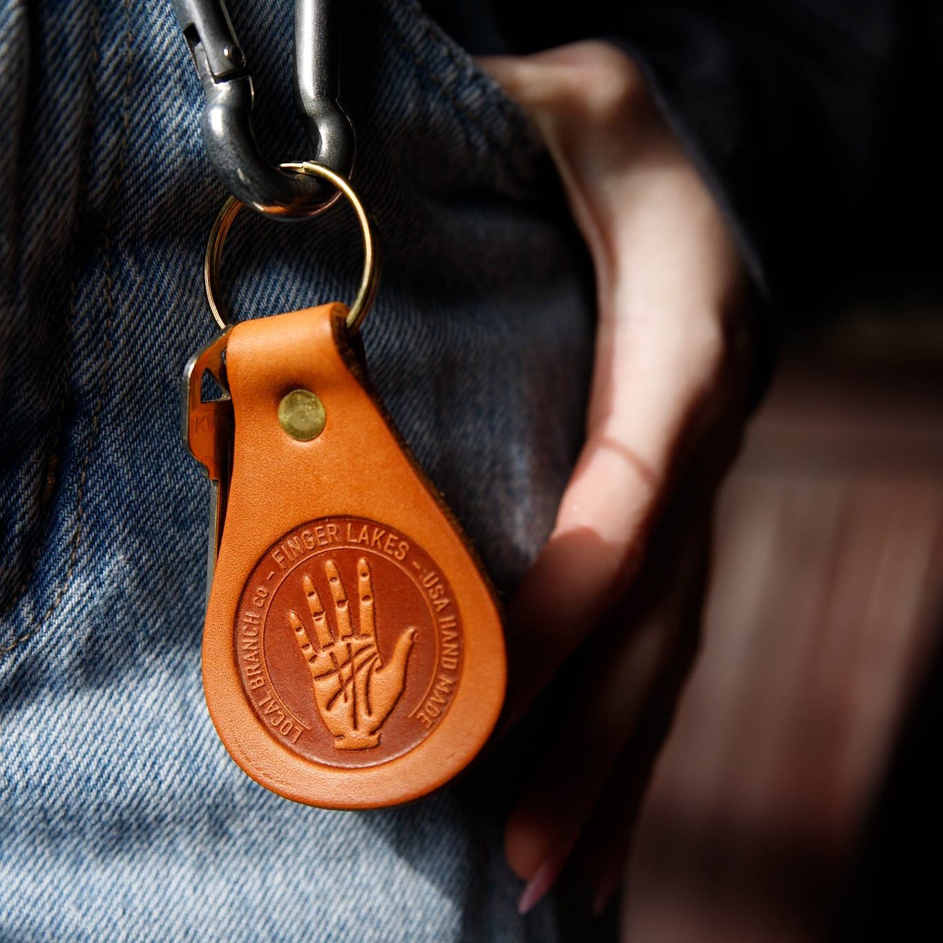 Brown leather keychain with embossed design attached to a keyring, held against a denim background.