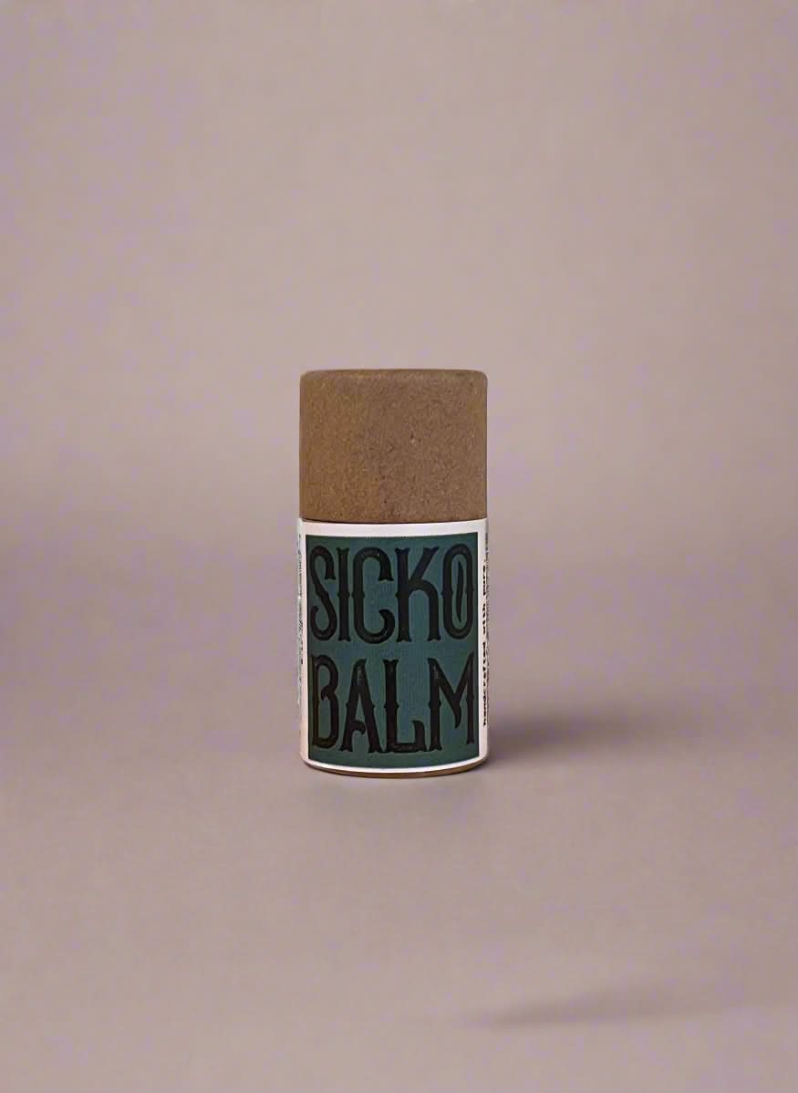 Stick of Sicko Balm on a wooden surface with a neutral background