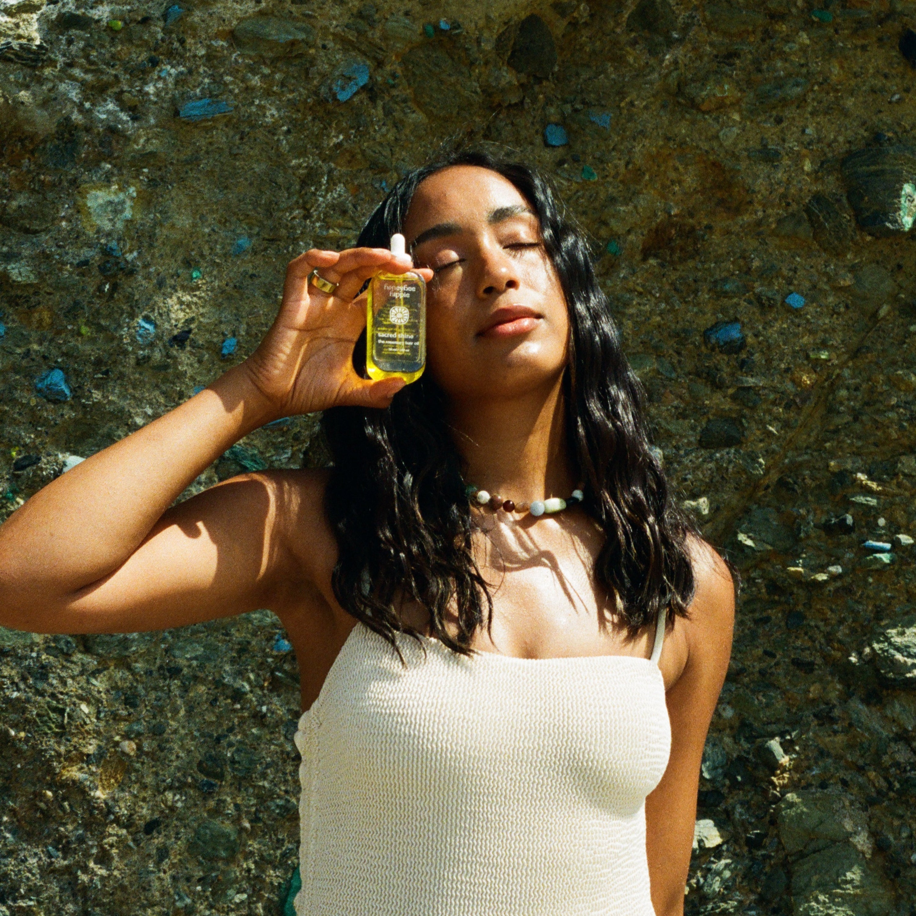 Woman holding a bottle of oil against a textured stone wall