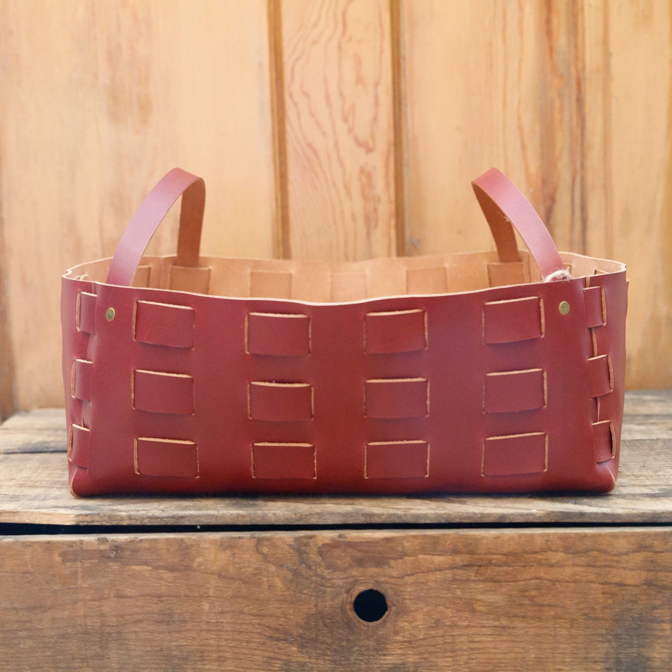 Red woven basket with leather handles on a wooden surface
