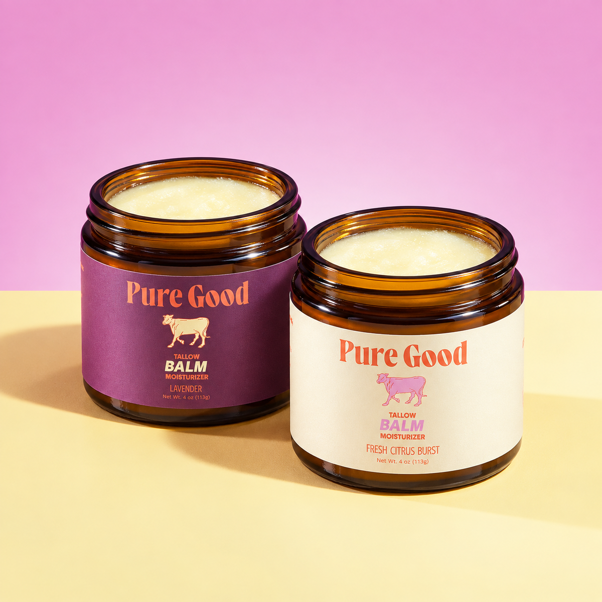 Two open amber glass jars of Pure Good Balm on a two-tone beige and pink background. The left jar has a purple label and contains a pale yellow balm, while the right jar has a white label and contains a pale cream balm.