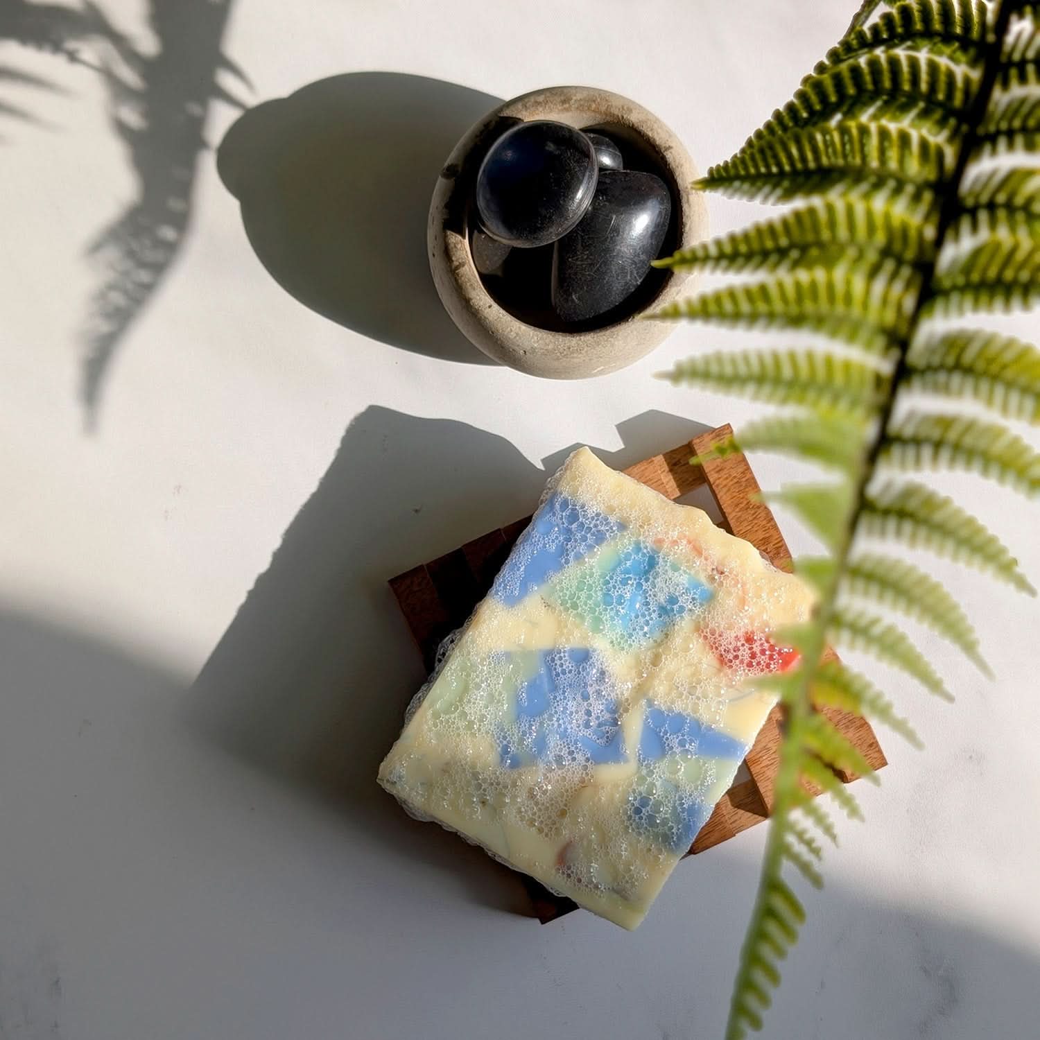 Colorful soap bar on a wooden block with a black candle and green plant in the background