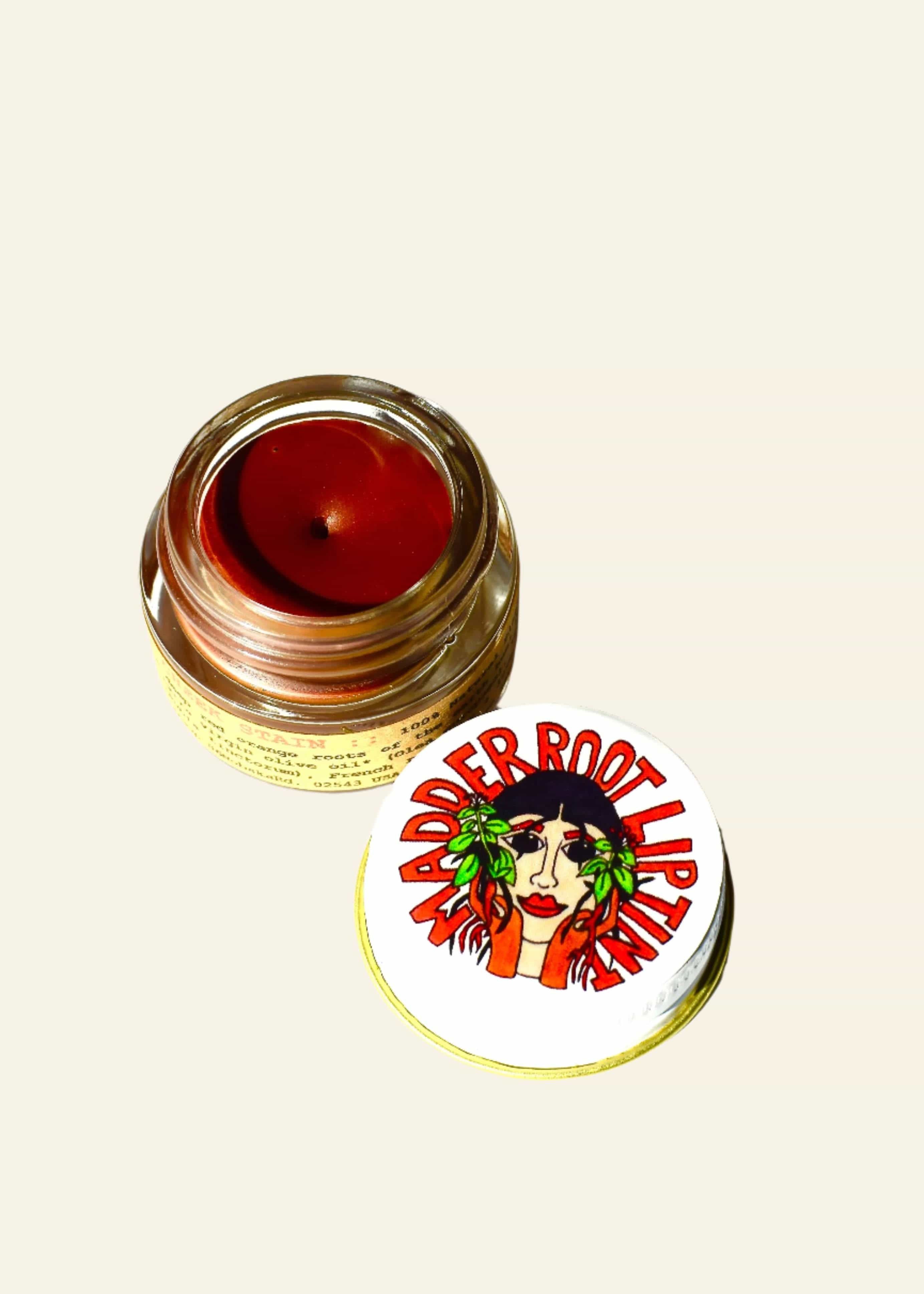 Jar of red lip balm with a label featuring a face and text on a white background