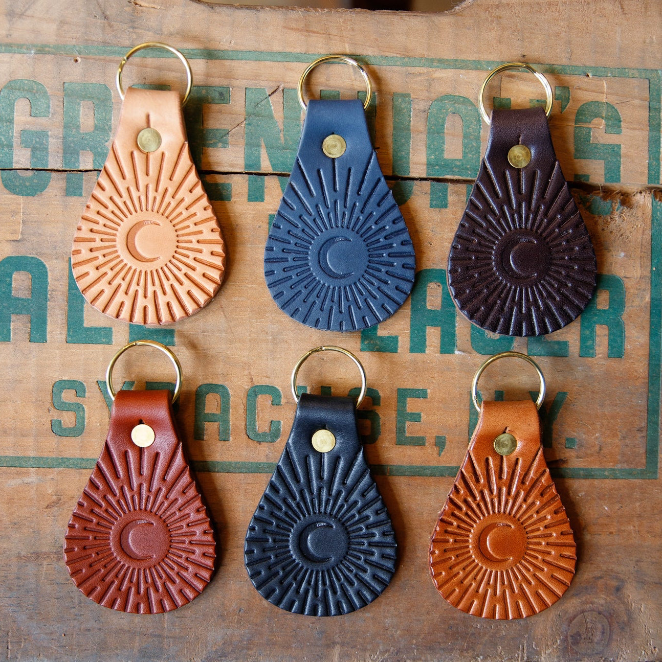 Set of six leather keychains with sunburst pattern on a wooden surface.