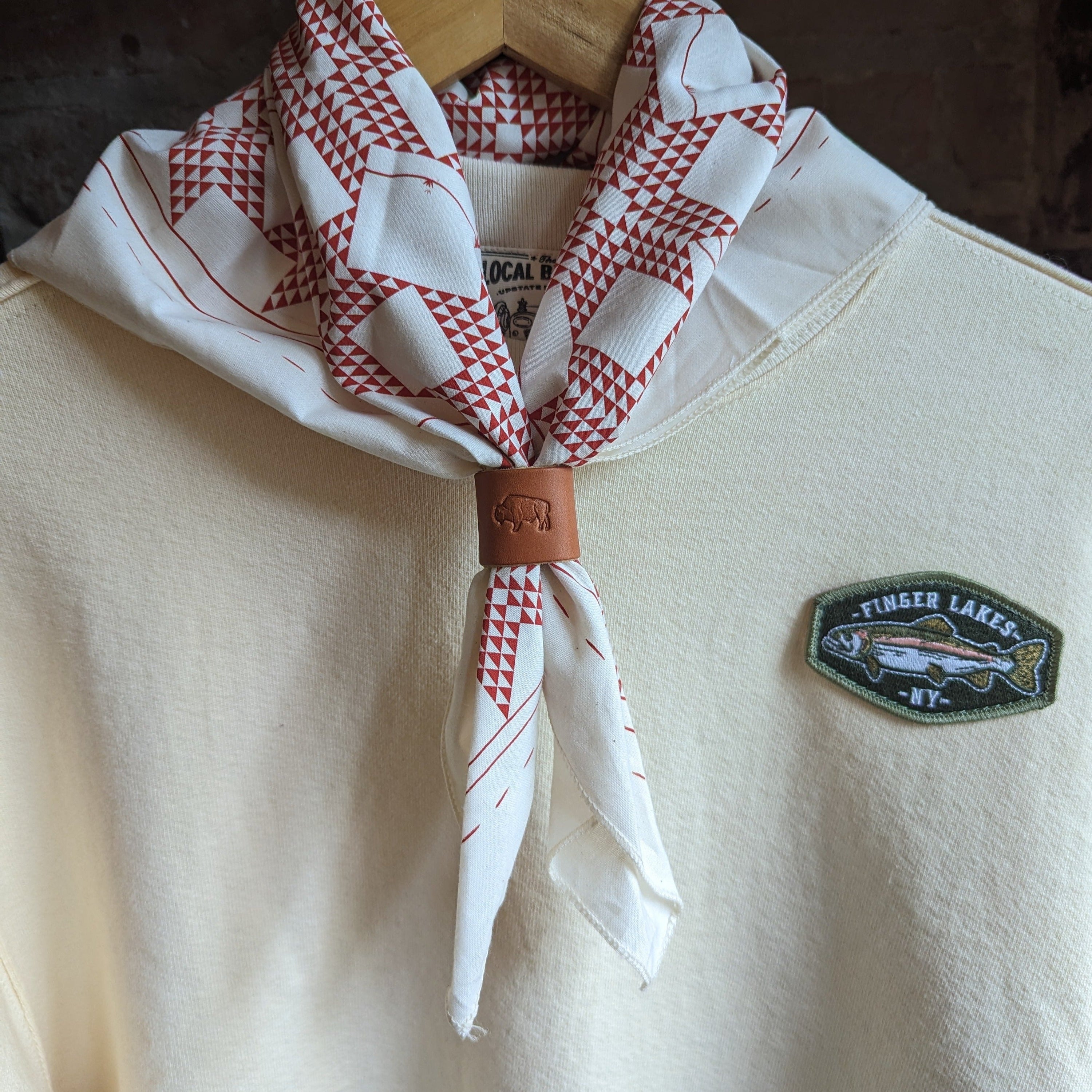 White shirt with red and white checkered scarf and fish patch on a wooden surface