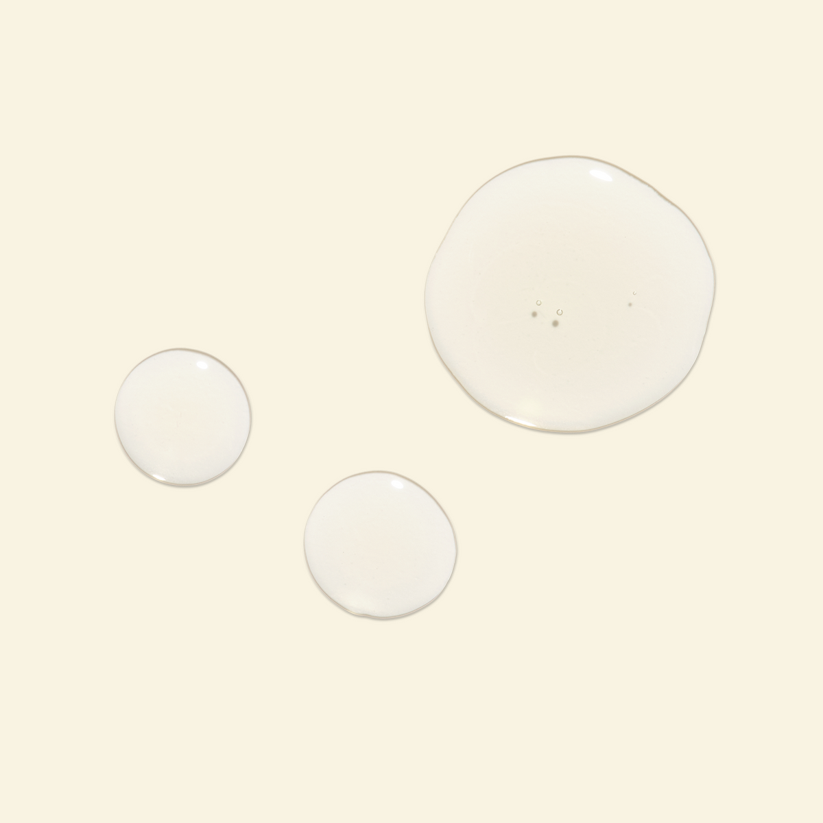 Three clear liquid droplets of varying sizes on a solid pale cream background.