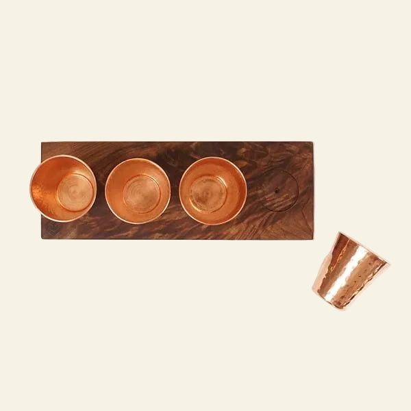 Wooden tray with three copper bowls and a fourth copper cup on a white background