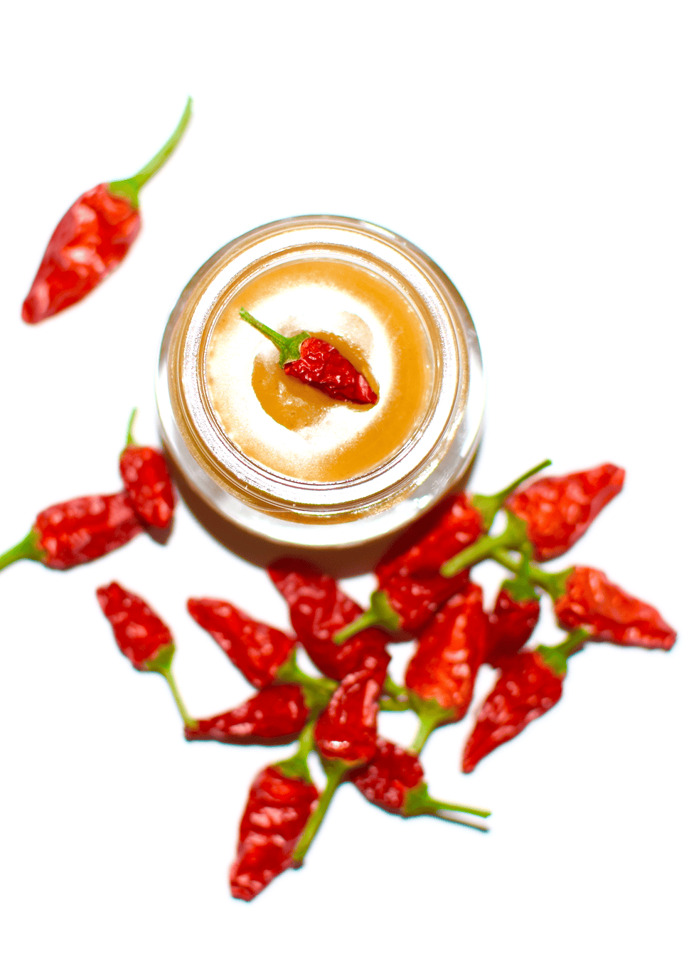 Jar of cream with a red chili pepper on top, surrounded by red chili peppers on a white background