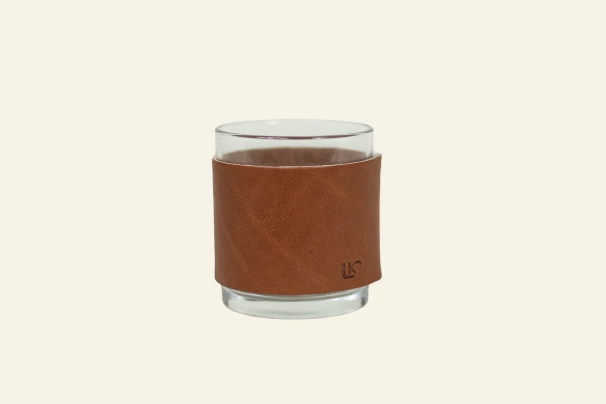 Glass tumbler with a brown leather sleeve on a white background