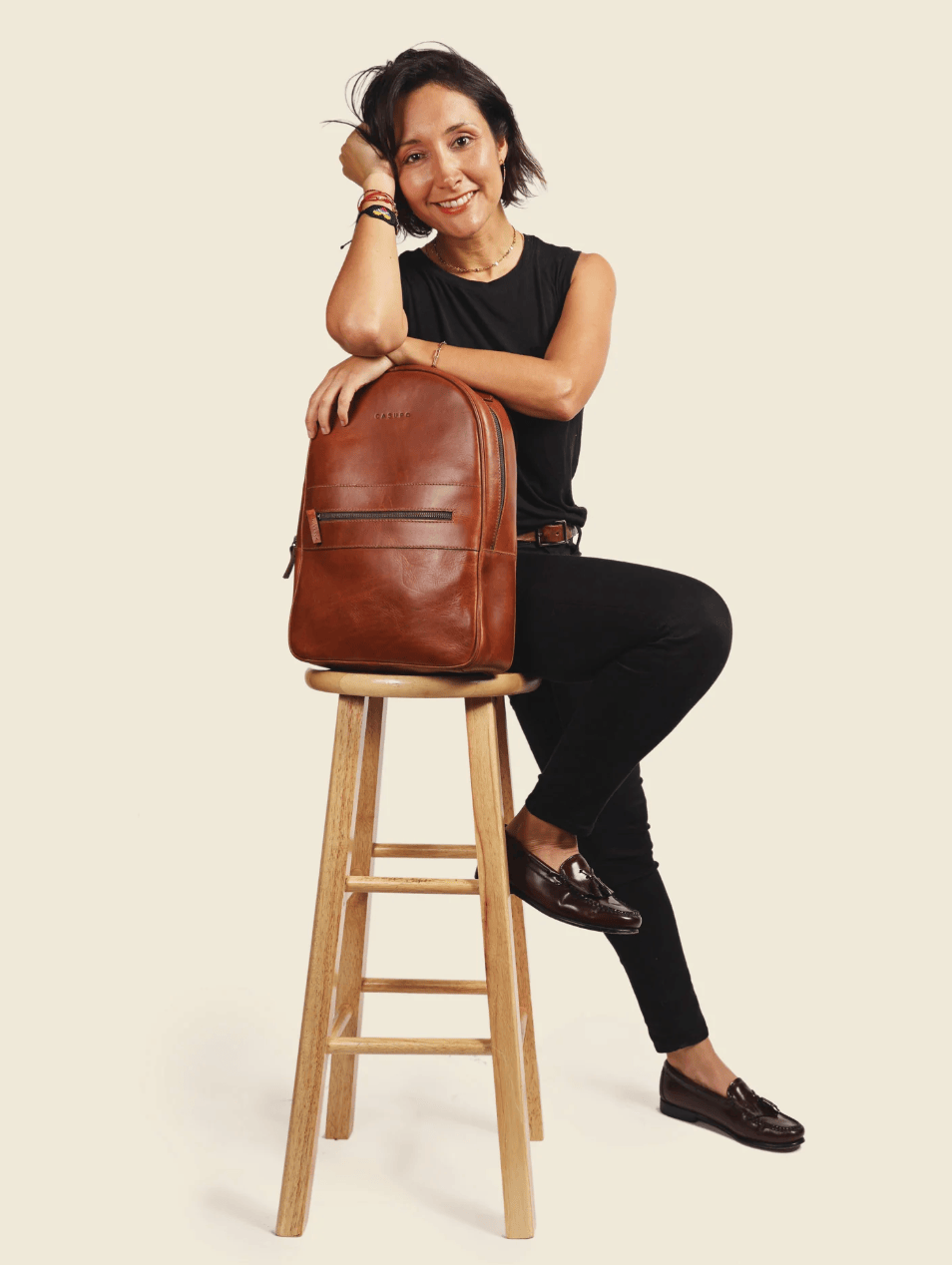 Woman sitting on a wooden stool with a brown leather backpack