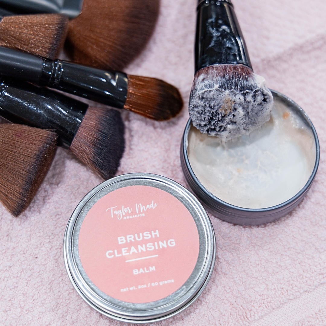 Makeup brushes with a jar of brush cleansing balm on a pink surface