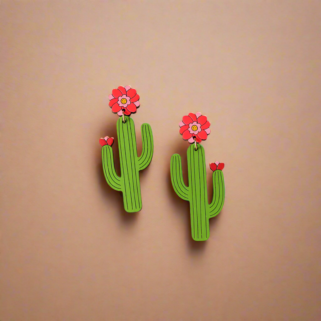 Cactus-shaped earrings with pink flowers on a heart-shaped dish with pink flowers in the background