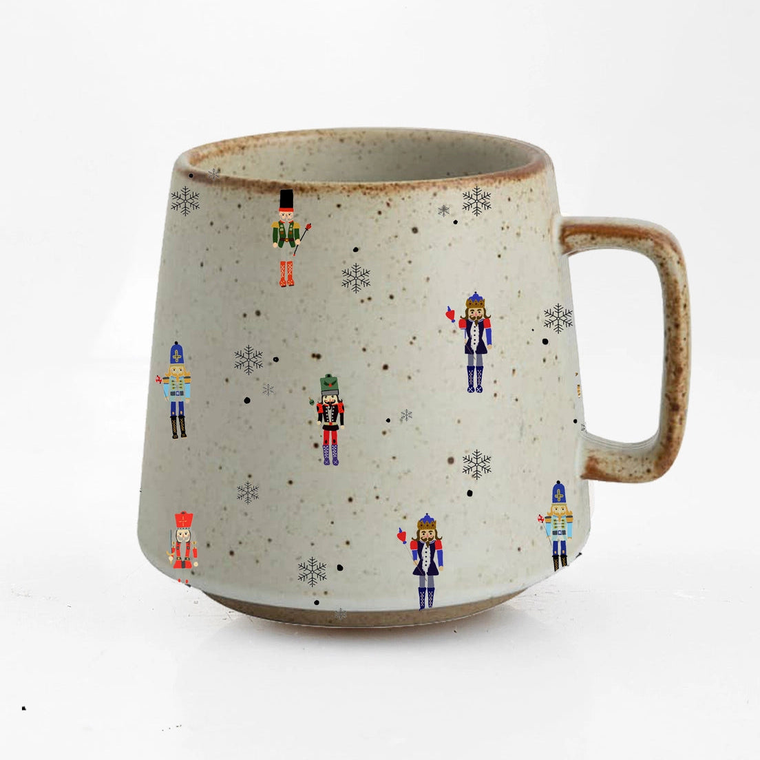 A speckled ceramic mug with a handle, decorated with small colorful nutcracker figures and snowflakes on a light gray background, set against a plain white studio backdrop.