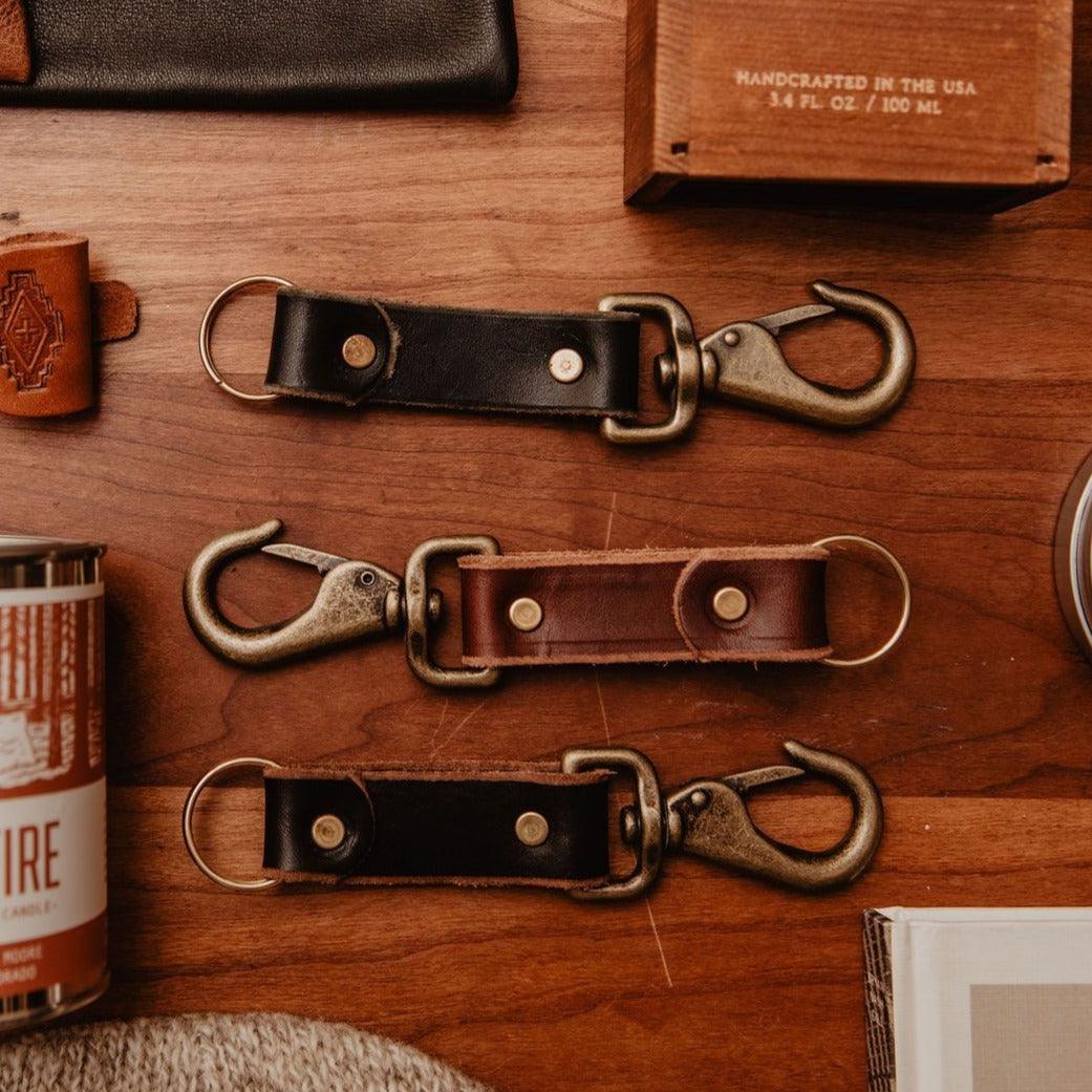 Three leather keychains with metal hooks on a wooden surface.
