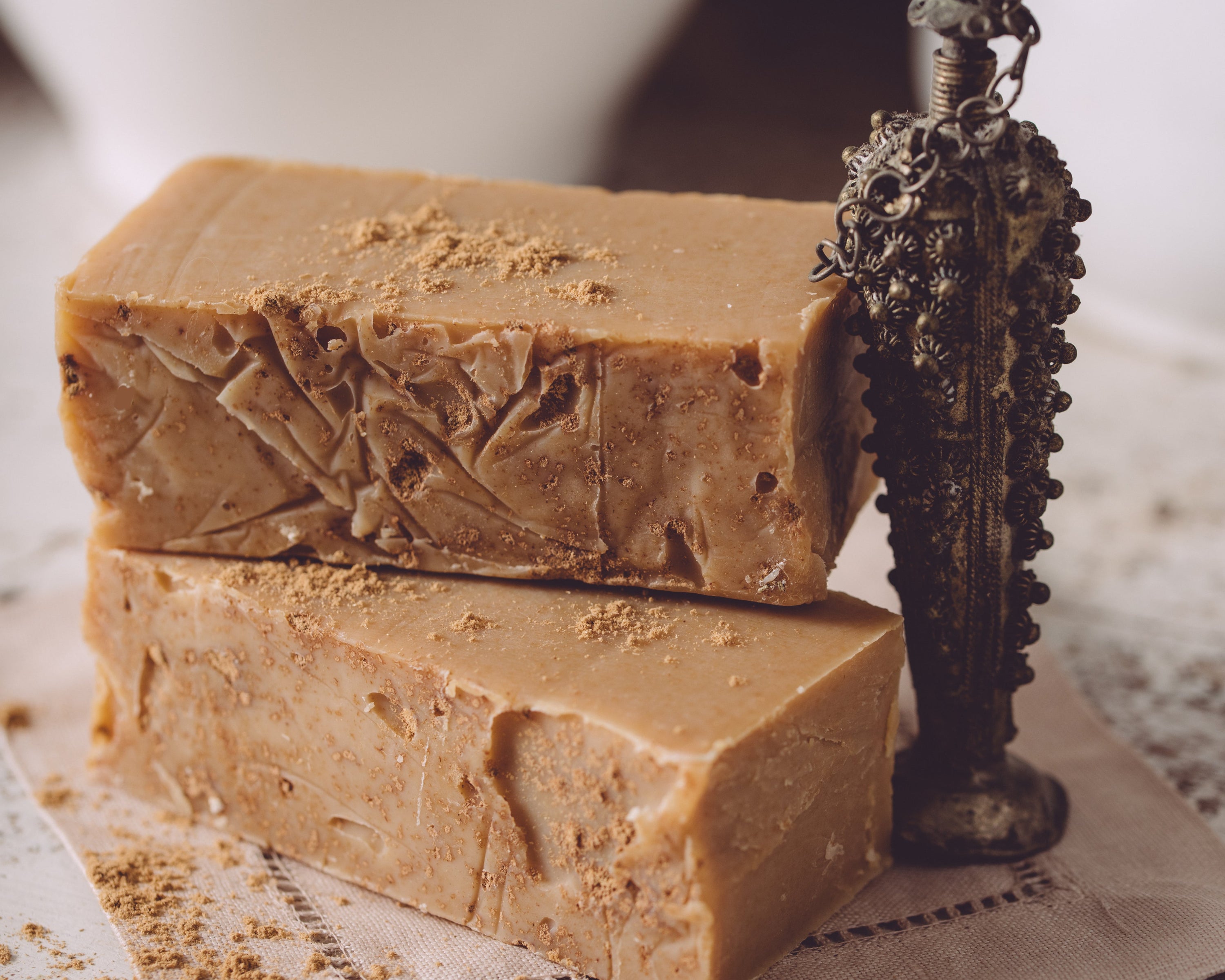 Two bars of brown soap with a decorative metal object on a textured surface.