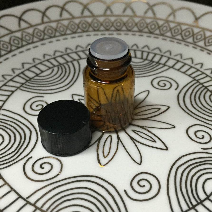 Small amber glass bottle with a black cap on a decorative white plate with black patterns