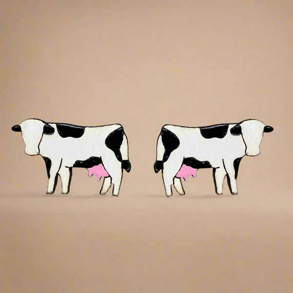 Two black and white cow earrings with pink udders on a beige background