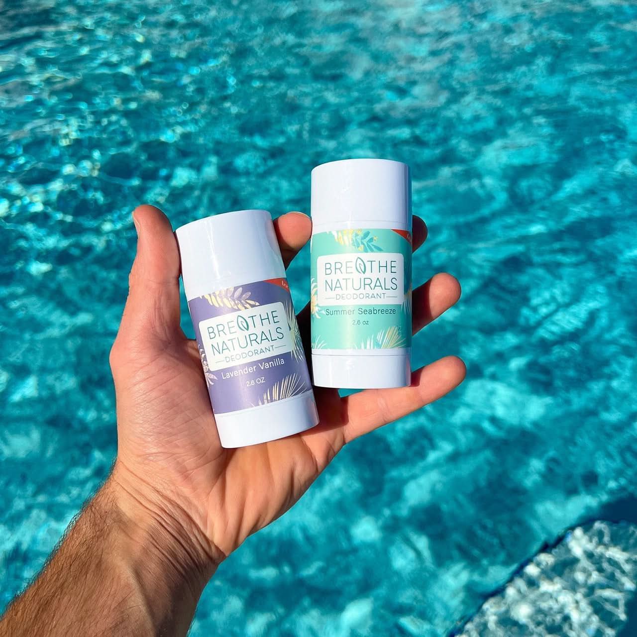 Two deodorant sticks from Breathe Naturals held in front of a pool.