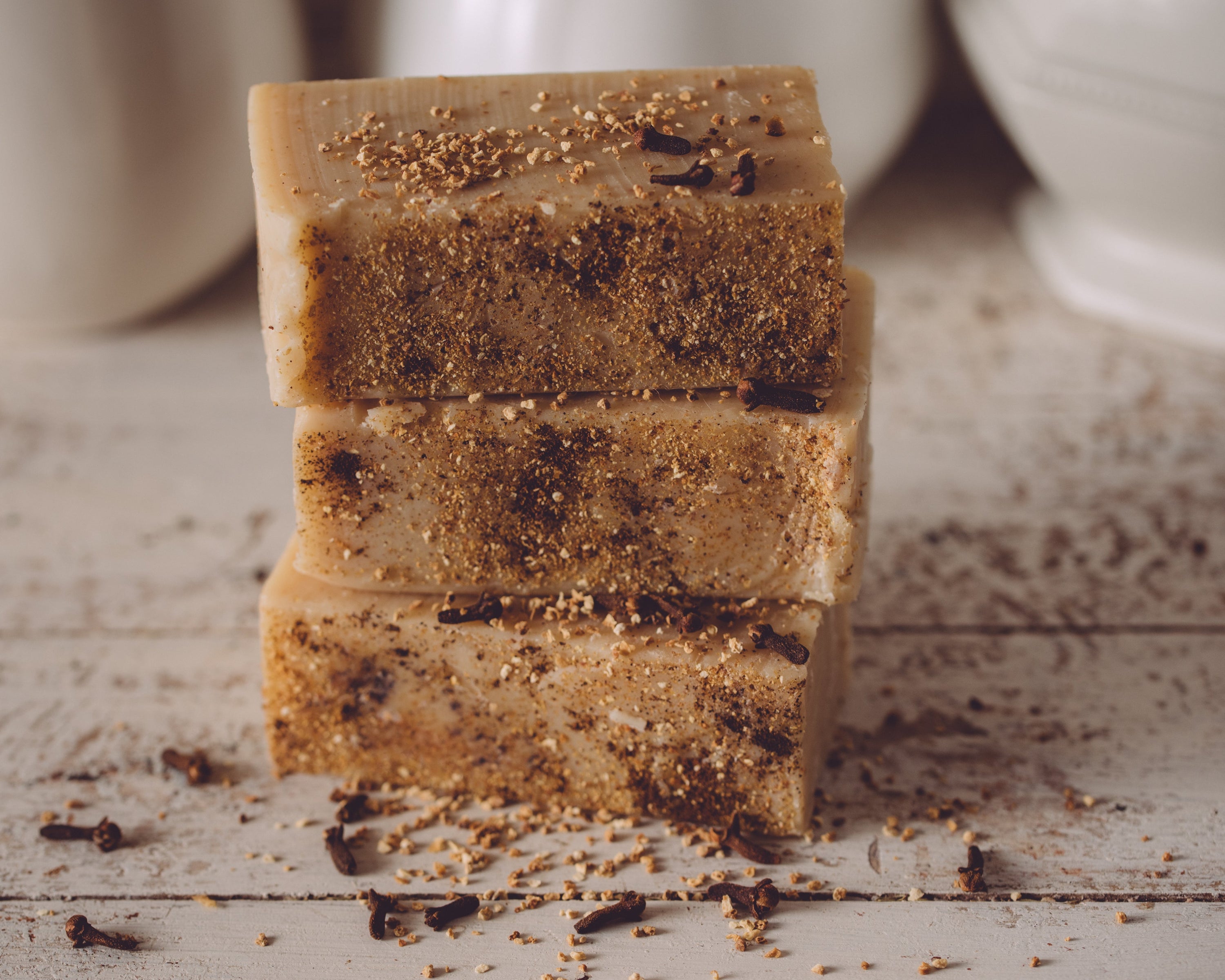 Stack of three brown soap bars with specks on a wooden surface