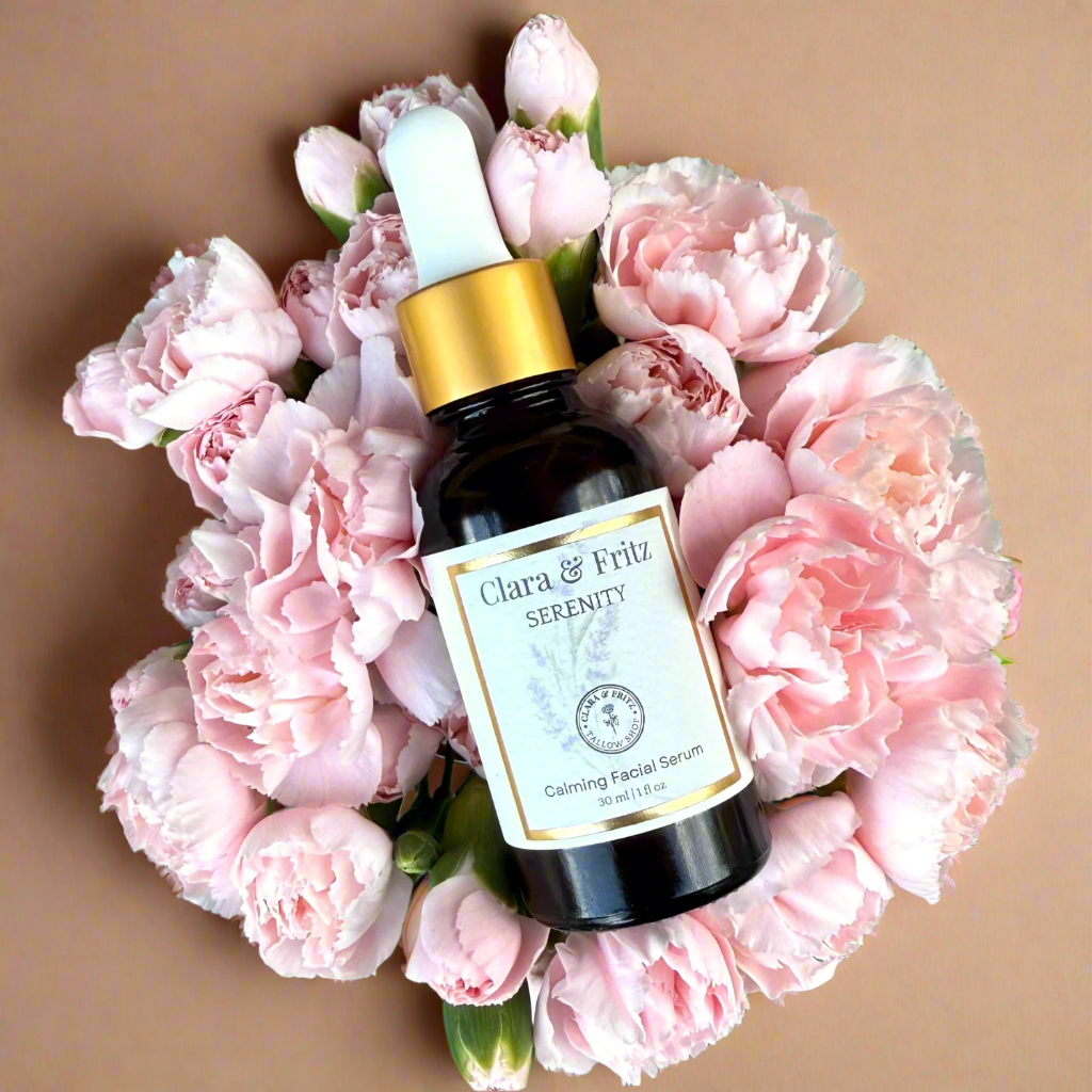 Bottle of Clara & Fritz Serenity Calming Facial Serum surrounded by pink flowers on a green background