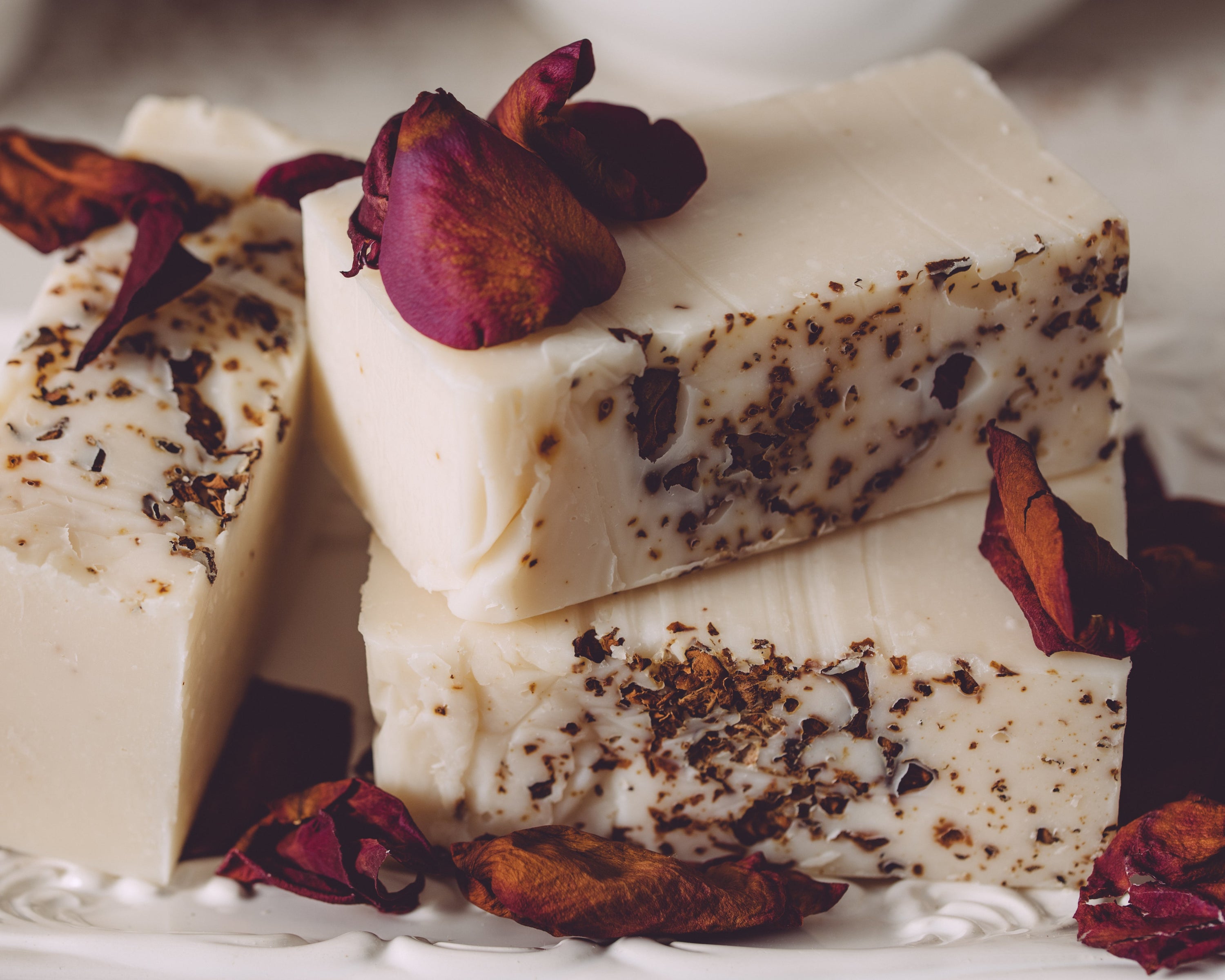Three pieces of white soap with dark specks, garnished with dried red flowers on a white surface.