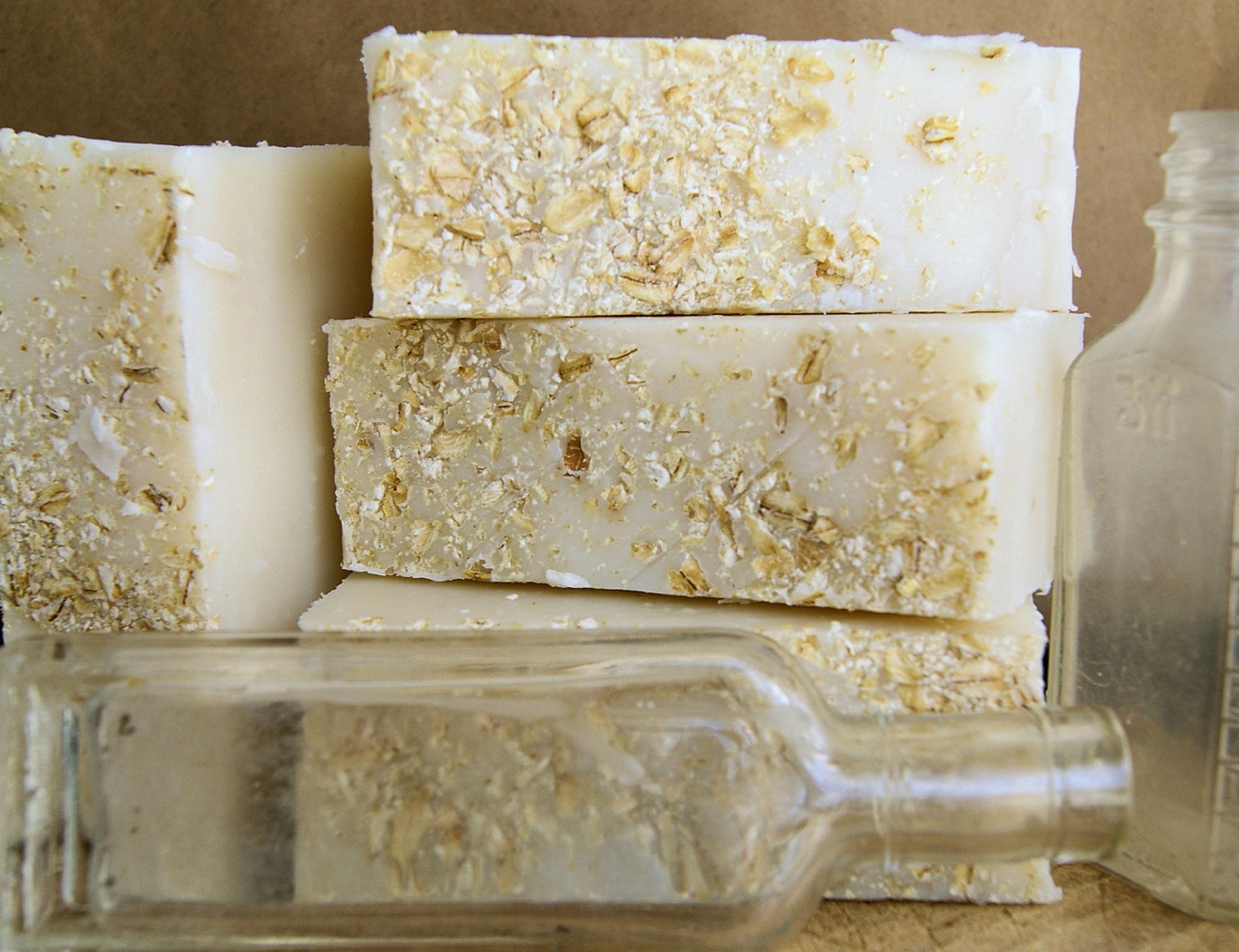 Three bars of soap with oatmeal pieces on a reflective surface