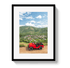 Framed photograph of a red jeep on a dirt road with mountains and town in the background.