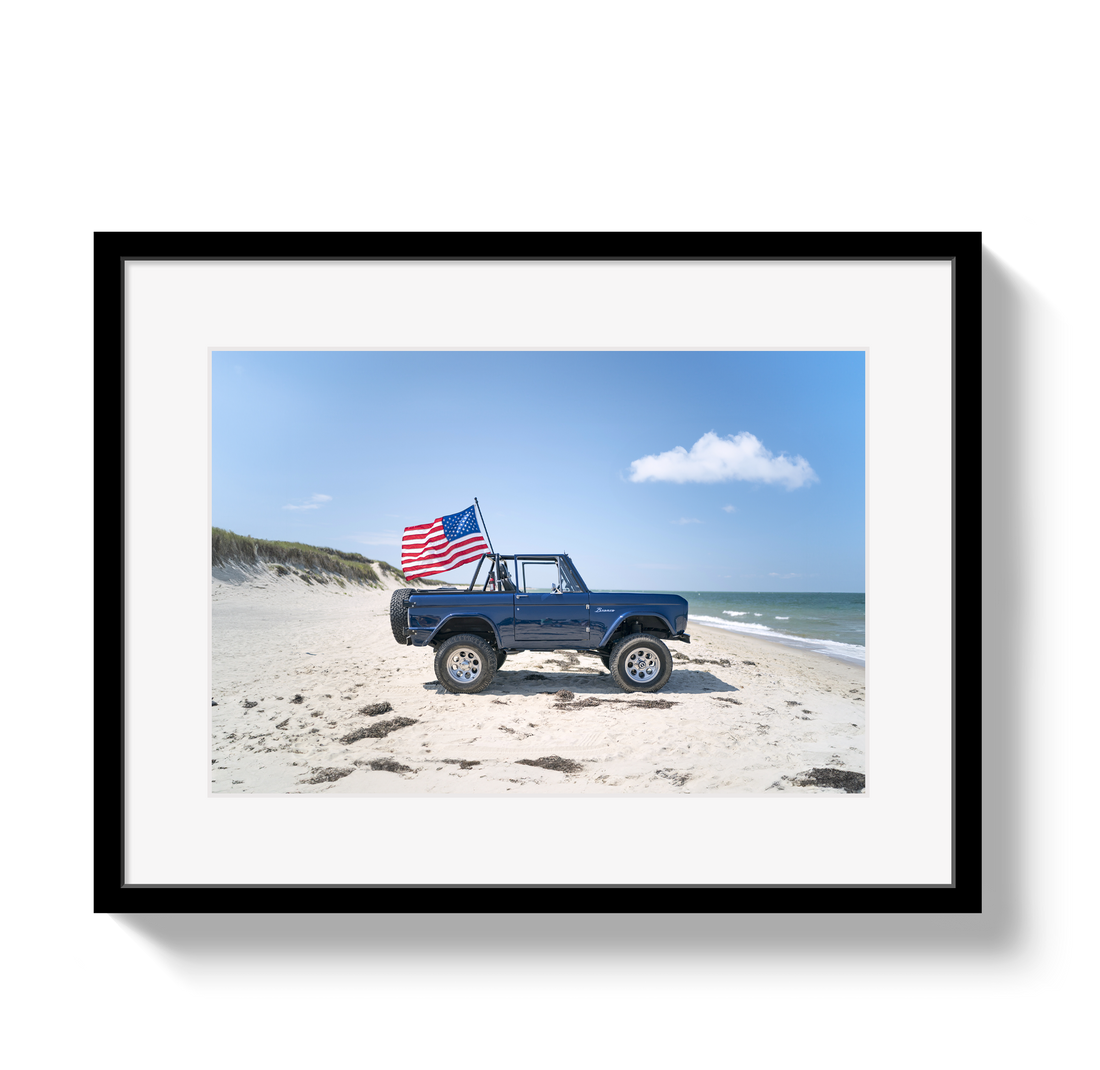 Framed photo of a blue truck with an American flag on a beach