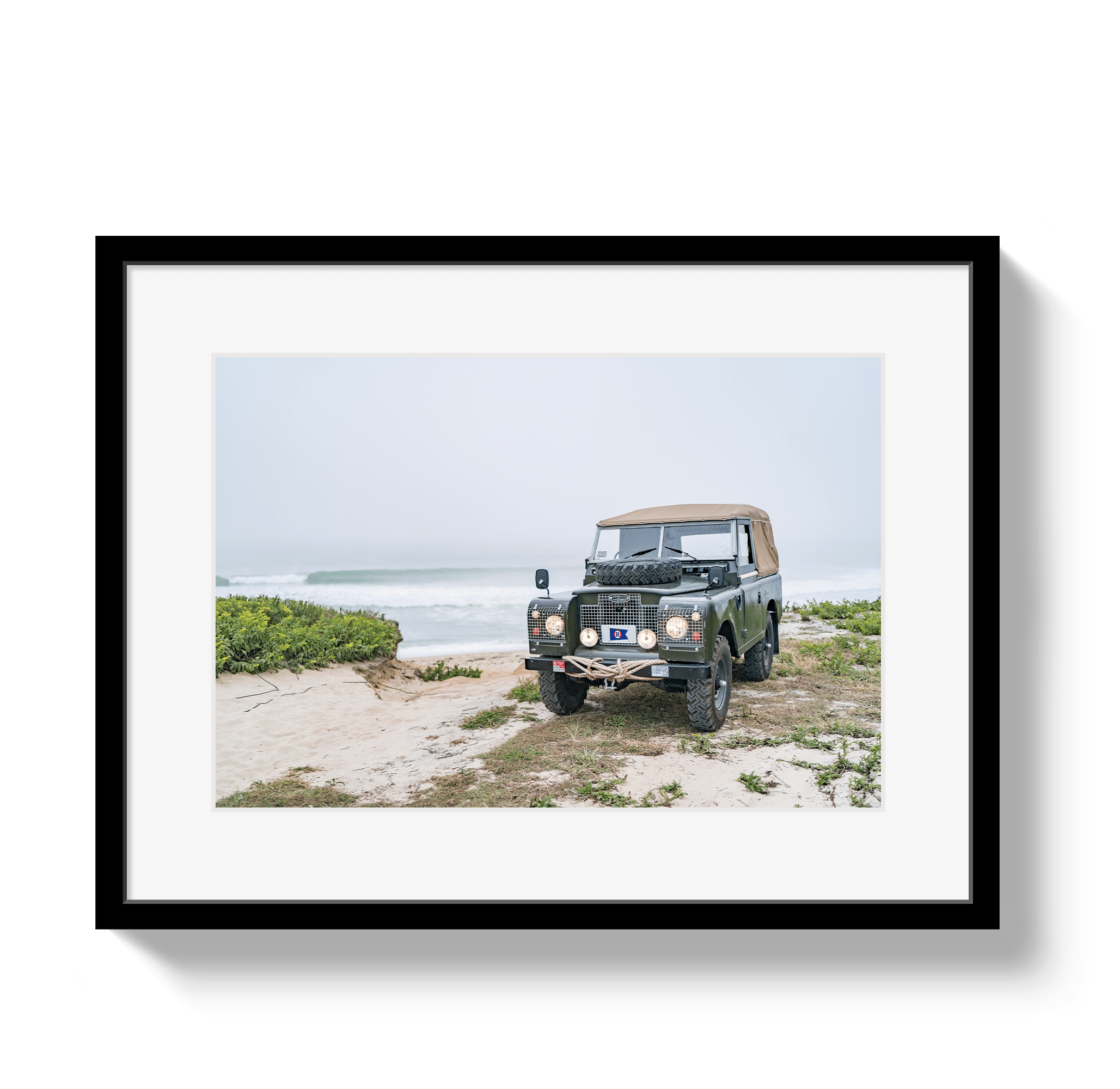 Framed photograph of a vintage Land Rover on a beach with a black frame.