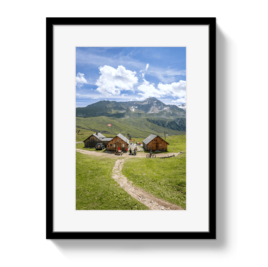 Framed picture of a mountain landscape with wooden cabins and a dirt path.