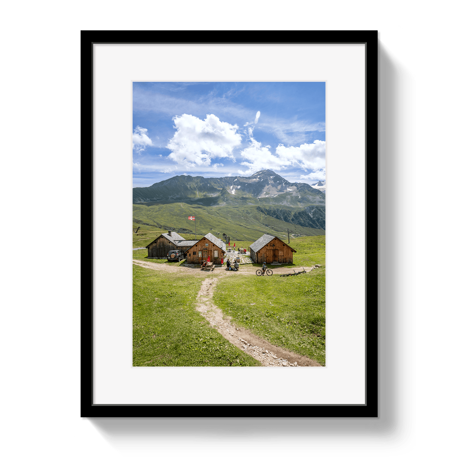 Framed picture of a mountain landscape with wooden cabins and a dirt path.