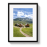 Framed picture of a mountain landscape with wooden cabins and a dirt path.